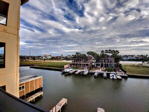 A waterfront property with a dock, a building with multiple levels, and a clear sky. - Landfall Towers #34 - Stunning Bayfront Living with Private Boat Slip Access (South Padre Island)