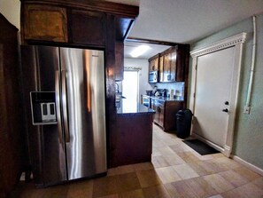 Eine Küche mit einem Edelstahl-Kühlschrank, Holzschränken, einer Mikrowelle und einem Mülleimer.