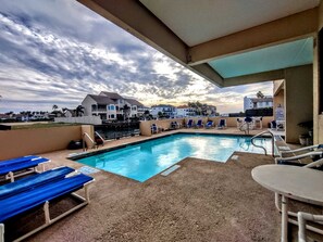 A swimming pool with lounge chairs and a view of houses in the background. - Landfall Towers #71 - Breathtaking Bayfront Living with Boat Slip Access (South Padre Island)