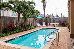 A swimming pool with a wooden fence, palm trees, and a patio area with chairs and a table. - Tropical 2-BR Family Sanctuary at Lantana Landing #1 - Walk to Beach & Dining (South Padre Island)