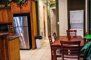 A kitchen with wooden cabinets, a stainless steel refrigerator, a dining table with chairs, and a white stove. - Tropical 2-BR Family Sanctuary at Lantana Landing #1 - Walk to Beach & Dining (South Padre Island)