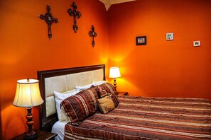 Ett hotellrum med en säng, två sänglampor, en sänggavel och tre kors som hänger på väggen.