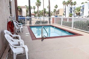 Ein Swimmingpool mit weißem Zaun, weißen Stühlen und Palmen im Hintergrund.