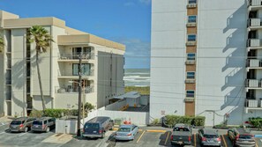 Un immeuble à plusieurs étages doté de balcons donnant sur un parking et offrant une vue sur l’océan.
