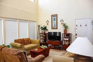 Ein Wohnzimmer mit einer Couch, Fernseher, Couchtisch und Zimmerpflanzen.