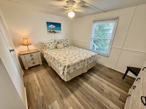 Un dormitorio con cama, mesita de noche, lámpara y ventana con persianas.