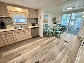 A kitchen with wooden cabinets, a sink, and a dining area with chairs and a table. - Pet-Friendly Ocean Lakes 4BR | Limo Golf Cart | Sleeps 9 (Myrtle Beach)