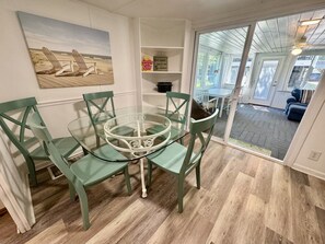 A dining area with a glass table and green chairs, a beach-themed painting, and a view through a glass door to an outdoor deck. - Pet-Friendly Ocean Lakes 4BR | Limo Golf Cart | Sleeps 9 (Myrtle Beach)
