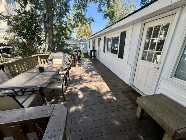 En takförsedd veranda med picknickbord och stolar, en träbänk och ett vitt, flyttbart hus med fönster och dörrar.