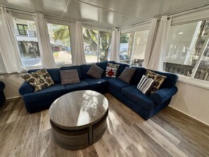 A modern living room with a sectional sofa, a round coffee table, and large windows. - Pet-Friendly Ocean Lakes 4BR | Limo Golf Cart | Sleeps 9 (Myrtle Beach)
