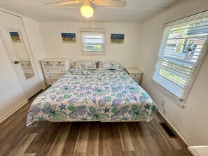 A bedroom with a bed, a nightstand, a dresser, a ceiling fan, and a window with blinds. - Pet-Friendly Ocean Lakes 4BR | Limo Golf Cart | Sleeps 9 (Myrtle Beach)