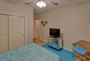 Ein Schlafzimmer mit einem Bett, einem Fernseher auf einem Schrank, einem Sessel und einem Deckenventilator.