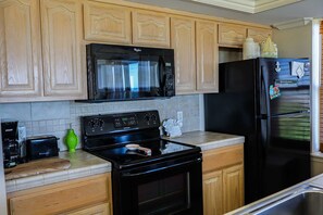 A kitchen with wooden cabinets, a black microwave, a black refrigerator, and a stove. - Seagull #101 - Expansive Gulf Views in a Private Beachfront Sanctuary (South Padre Island)