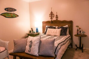 A bedroom with a bed, pillows, a nightstand, a lamp, a chair, and wall decorations. - Seagull #101 - Expansive Gulf Views in a Private Beachfront Sanctuary (South Padre Island)