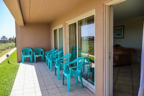 A covered outdoor seating area with turquoise plastic chairs and a tiled floor. - Seagull #101 - Expansive Gulf Views in a Private Beachfront Sanctuary (South Padre Island)