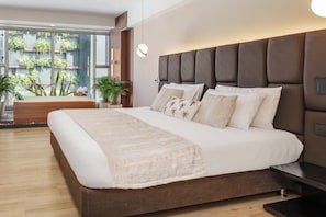 Un dormitorio moderno con una cama grande, un banco de madera y vistas a zonas verdes.