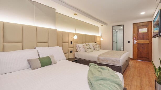 Quarto de hotel com duas camas, piso de madeira, uma porta e um espelho.