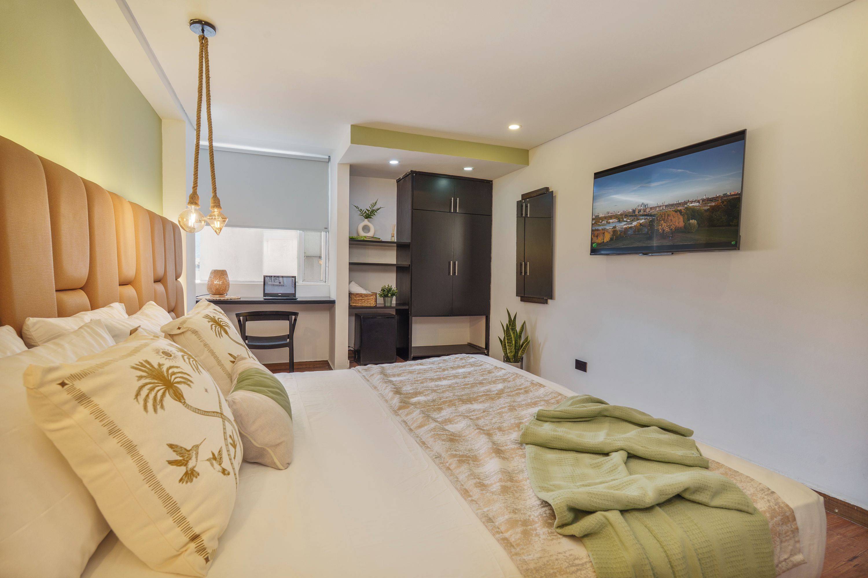 A modern bedroom with a large bed, a desk, and a cityscape view.