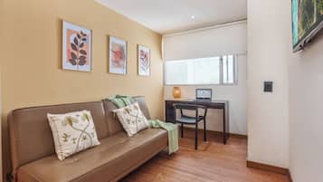 Ein Wohnzimmer mit einem braunen Ledersofa, zwei Zierkissen, einem kleinen Tisch mit einem Laptop und einem Fenster mit Blick.
