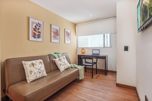Una sala de estar con un sofá de cuero marrón, dos almohadones decorativos, una mesita con una laptop y un ventanal con vistas.