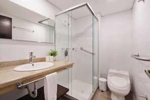 A modern bathroom with a glass-enclosed shower, a sink with a towel rack, and a toilet. - Veranova hotel (Medellín)