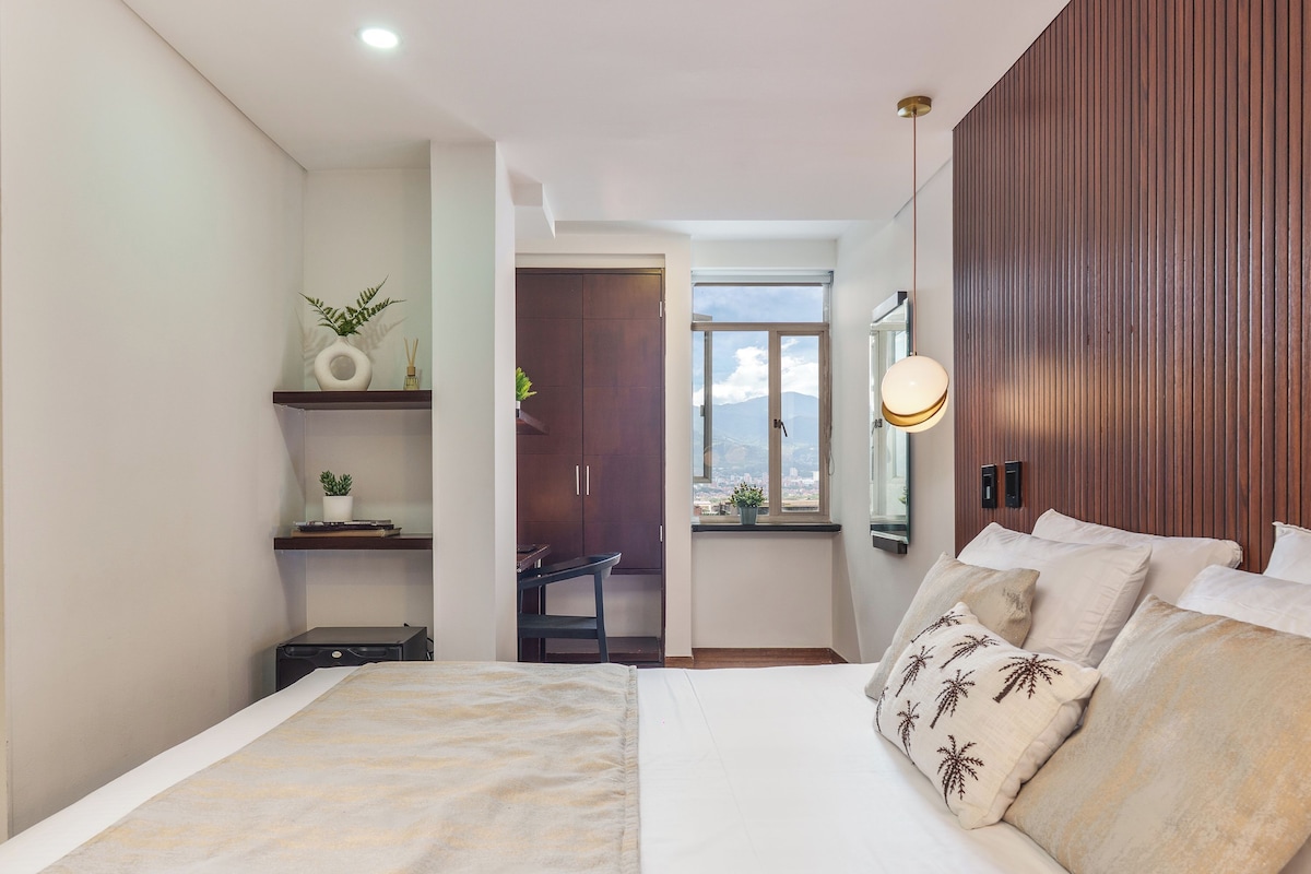 Un dormitorio con cama, mesita de noche, escritorio, silla, ventana con vistas y panel de pared de madera.