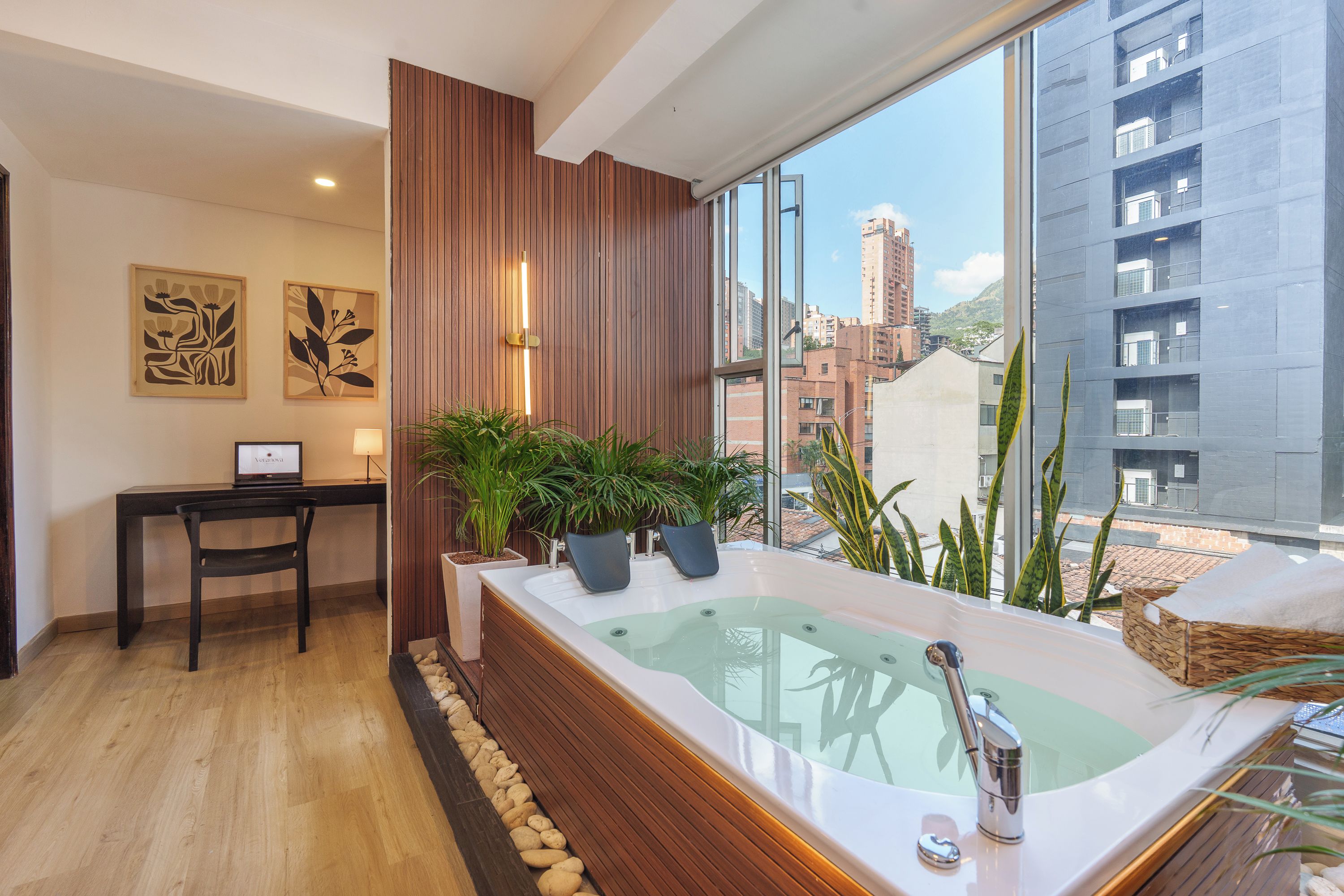 Un baño moderno con una bañera grande, paneles de madera, un escritorio con una computadora portátil y vistas a la ciudad.