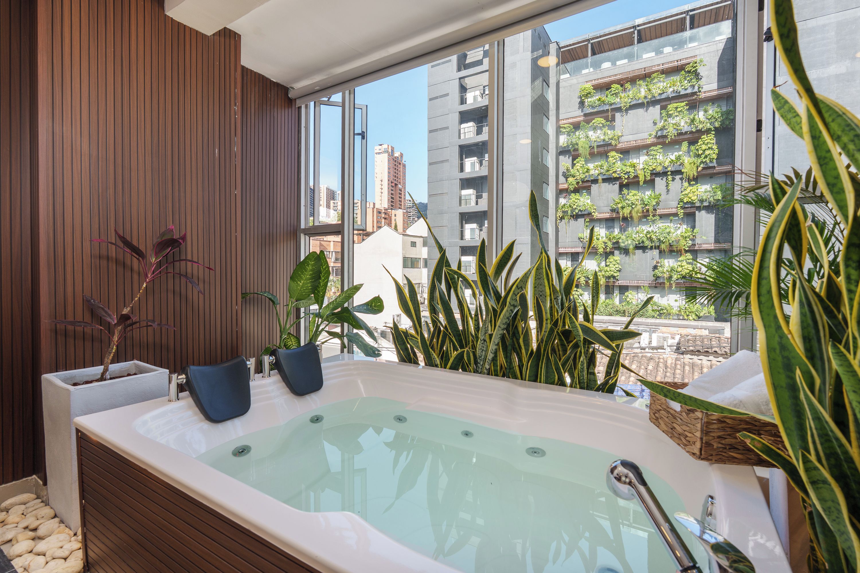 A modern bathroom with a large bathtub, wooden paneling, and a view of a cityscape through large windows.