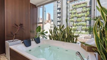 A modern bathroom with a large bathtub, wooden paneling, and a view of a cityscape through large windows.