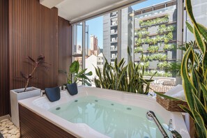 Een moderne badkamer met een groot bad, houten lambrisering en een stadsgezicht door grote ramen.