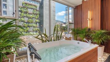 A modern bathroom with a large bathtub, wooden paneling, and a view of a cityscape through large windows.