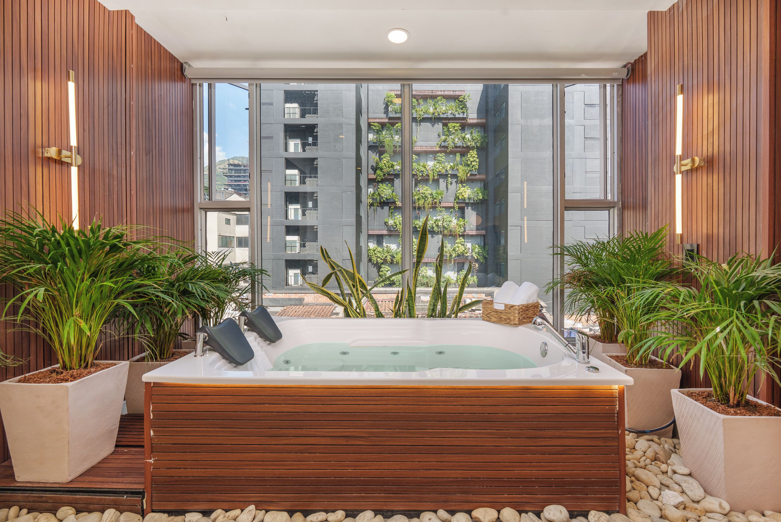 Ein Wellnessbereich mit Whirlpool, Topfpflanzen und Blick auf ein Gebäude mit Balkonen.