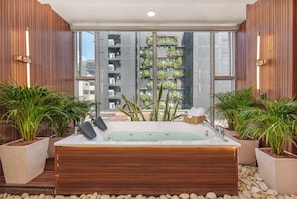 Zona de spa con un jacuzzi, plantas en macetas y vistas a un edificio con balcones.