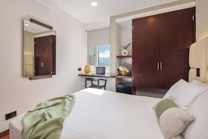 Una habitación de hotel con una cama, un escritorio con ordenador, un armario y un espejo.