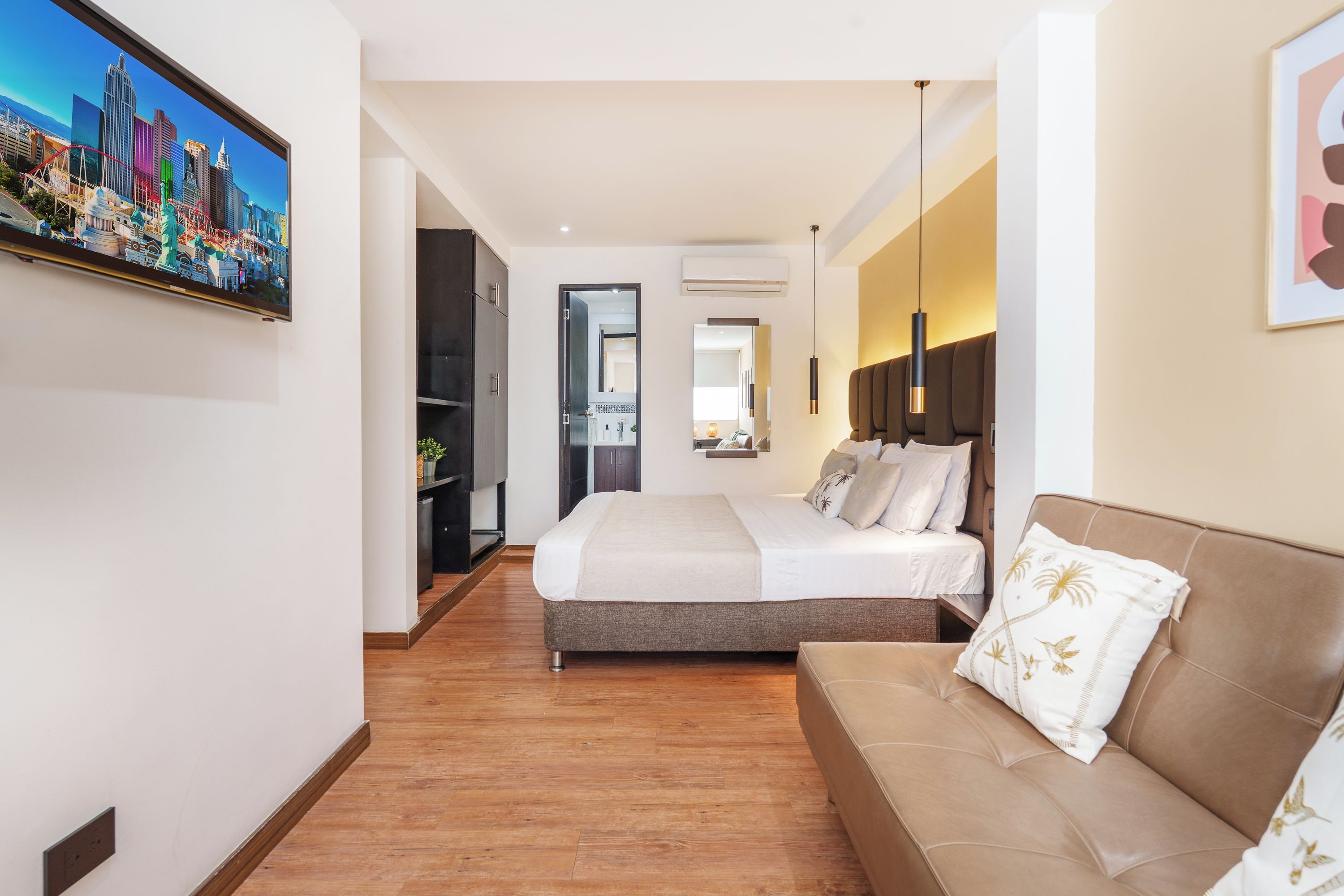 A hotel room with a bed, a sofa, a TV, and a cityscape view.