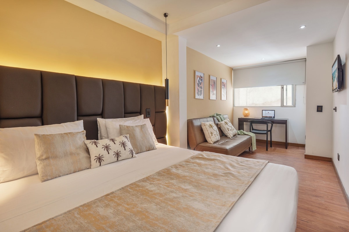 A modern hotel room with a large bed, a desk, and a sofa.