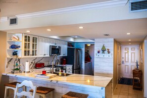 Una cocina moderna con armarios blancos, una isla central con taburetes, electrodomésticos de acero inoxidable y objetos decorativos en estantes.