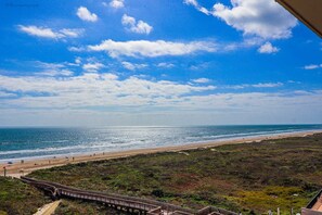 Eine Küstenlandschaft mit Strand, einem hölzernen Steg und blauem Himmel.