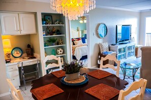 A dining area with a table set for four, surrounded by chairs, a central plant, and a decorative ceiling light. - Seville #602 - Premier Top-Floor Beachfront Living with Panoramic Gulf Views (South Padre Island)