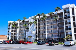 A multi-story hotel with a white facade, palm trees, and a clear blue sky. - Secure 3-BR Family Escape at Seville #603 - Beachfront with 2 Pools (South Padre Island)