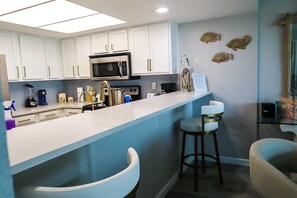 Una cocina moderna con gabinetes blancos, un microondas de acero inoxidable y una barra con taburetes.