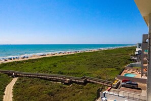 Blick auf einen Strand mit einer Holzpromenade, einem Poolbereich und blauem Himmel.