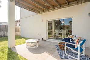 Ein überdachter Patio-Bereich mit einem runden Tisch, einer Couch mit Kissen und einem Korbstuhl.