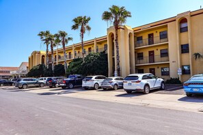 A multi-story hotel with a yellow facade, several balconies, and a parking lot with various cars. - Ventura #201 - 1/2 Block to the Beach Affordable 1-Bedroom Escape (South Padre Island)