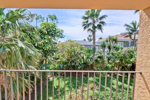 A balcony with a view of a lush garden, a metal railing, and a house in the background. - Ventura #201 - 1/2 Block to the Beach Affordable 1-Bedroom Escape (South Padre Island)