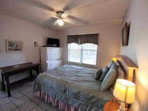 A bedroom with a bed, a desk, a chair, a ceiling fan, and a window with blinds. - Affordable 2-BR Retreat at Surfside 1 #206 - Just 2 Minutes to the Beach (South Padre Island)
