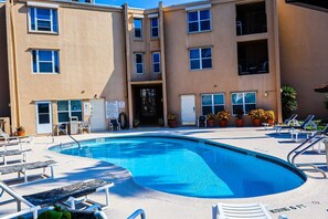 A swimming pool with lounge chairs and a building with multiple windows and doors. - Affordable 2-BR Retreat at Surfside 1 #206 - Just 2 Minutes to the Beach (South Padre Island)