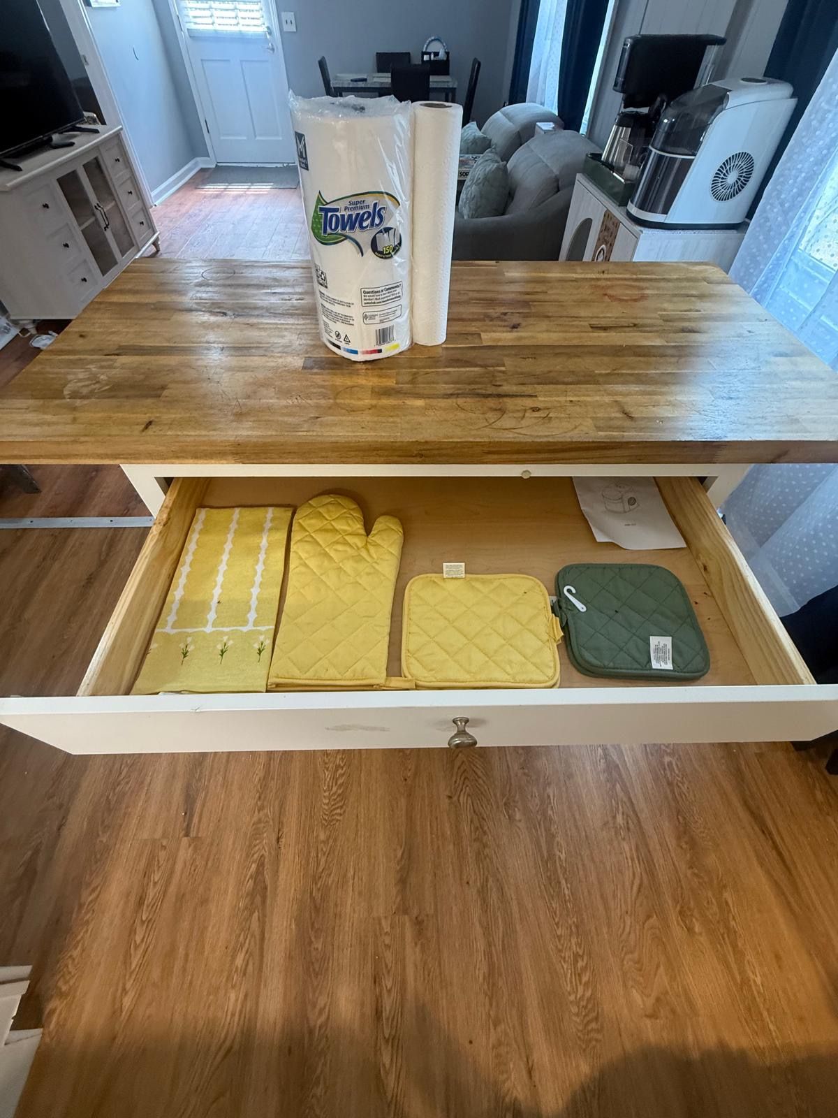 A kitchen area with a wooden countertop, a bag of paper towels, and a drawer containing kitchen utensils.