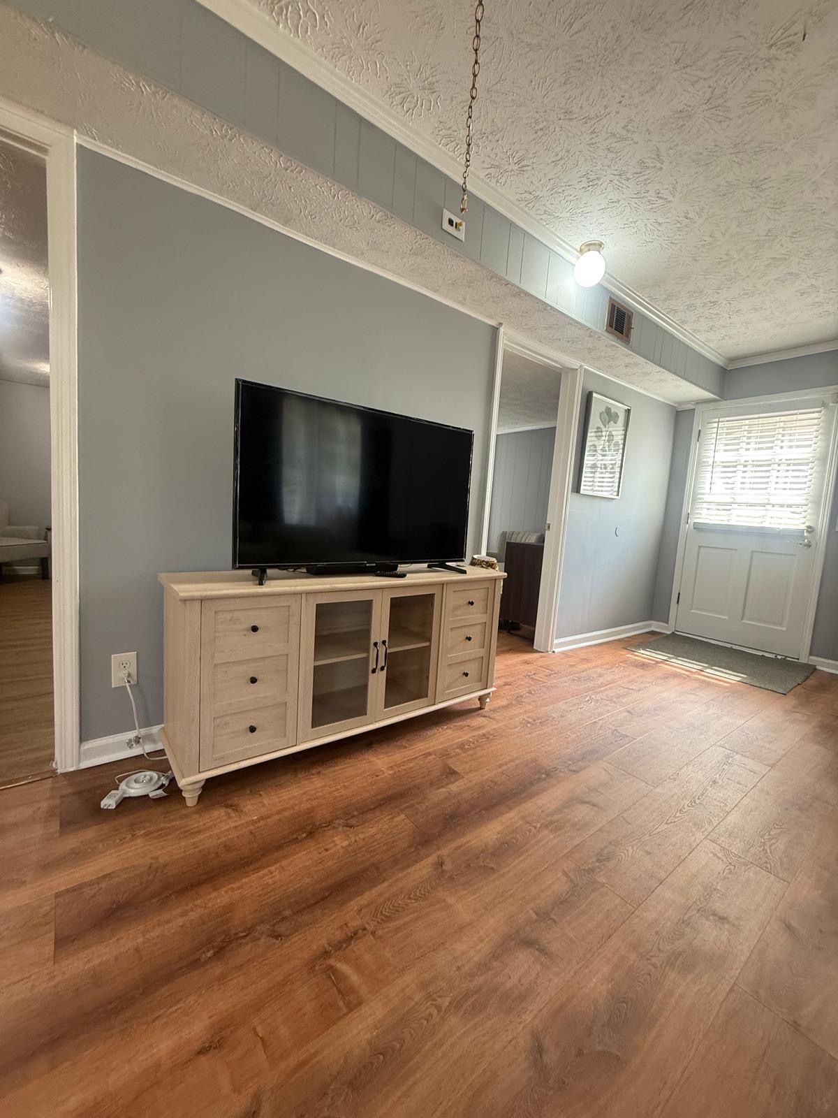 A room with a flat-screen TV on a wooden cabinet, a door with a window, and a ceiling fan.