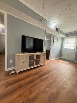 Una habitación con televisión de pantalla plana sobre un mueble de madera, una puerta con ventanal y un ventilador de techo.